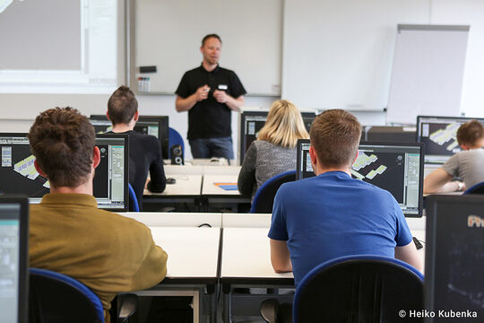 Ein Ausbilder hält einen Vortrag, während die Auszubildenden Teilnehmer vor Ihrem Computer sitzen und zuhören
